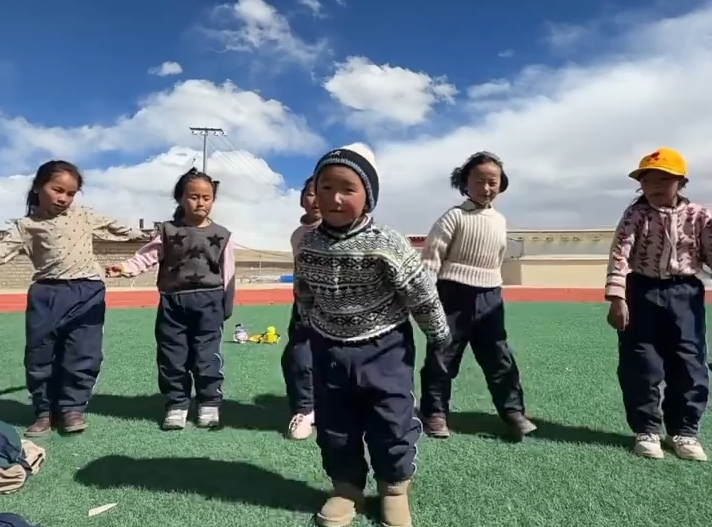 蓝天白云为伴，西藏萌娃在操场上跳锅庄 。
